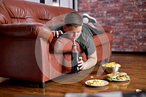 overweight obese boy is drinking carbonated sweet water beverage lying on sofa