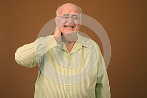 Overweight senior man wearing eyeglasses against brown background