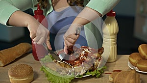 Overweight teenager carving chicken covered with ketchup and mayo and eating it