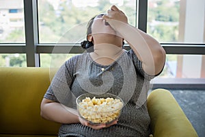 Overweight woman and asian girl enjoy eating food on sofa at home