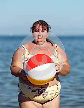 Overweight woman with ball on beach