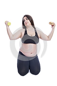 Overweight woman in black sportswear with dumbbells and a hamburger in her hands. Sports and diet in the fight against obesity.