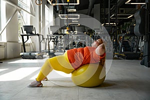 Overweight woman doing crunches exercise on fitness ball at gym