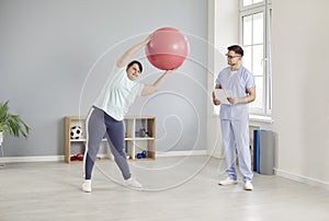 Overweight woman doing exercises with a fit ball under the control of a physiotherapist