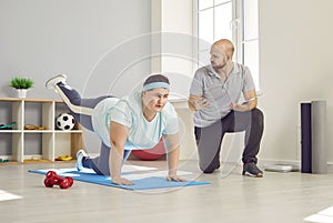 Overweight woman doing a plank with a leg raise during a sports workout with her trainer