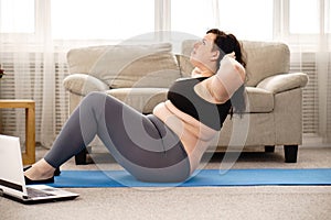 Overweight woman doing sit-ups on mat at home