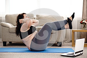 Overweight woman doing sit-ups on mat at home