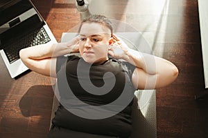 overweight woman doing sit-ups on mat at home