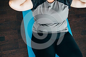 Overweight woman doing sit-ups on mat indoors