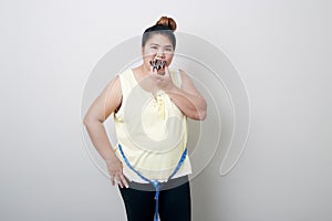 Overweight woman eating food on gray background