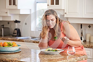 Overweight Woman Eating Healthy Meal In Kitchen