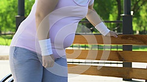 Overweight woman exhausted after tiresome workout outdoors, resting on bench