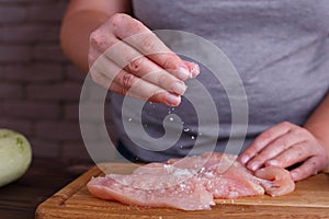 Overweight woman hands adding salt to raw chicken breasts. Dieti