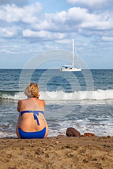 Overweight woman on her back, sitting on the beach sand.