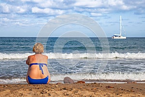 Overweight woman on her back, sitting on the beach sand.