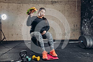 Overweight woman holding hamburger and looking at the camera