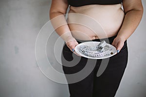 Overweight woman holding plate with measure tape