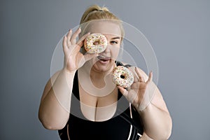 A overweight woman is holding two sweet glazed bagels in her hands and can`t resist eating them.