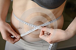Overweight woman measures her waist with excess weight on her stomach with a measuring tape. Concept of weight loss