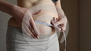 An overweight woman measures her waist with a measuring tape, then holds excess fat on her stomach with her hands