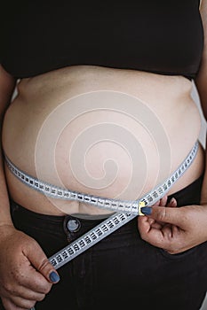 Overweight woman measuring waist with measure tape