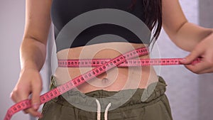 Overweight woman measuring waist with tape measure close up