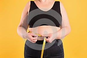 Overweight woman measuring waist with tape on yellow background, closeup