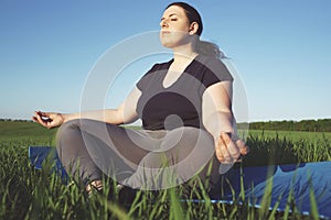 Overweight woman meditating at yoga mat outdoors