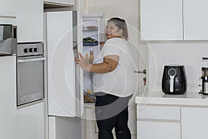 Overweight woman opening a refrigerator at home