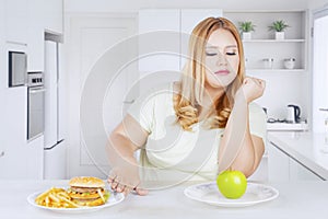 Overweight woman rejecting fast foods in kitchen