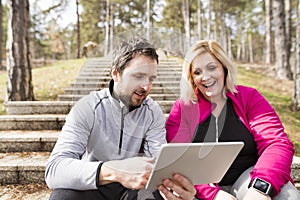 Overweight woman resting after run, personal trainer checking her profile, performance on tablet. Exercising outdoors