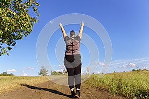 Overweight woman rising hands, view from the back