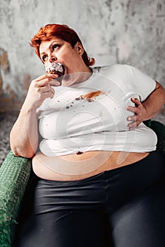 Overweight woman sits in chair and eats sweet cake