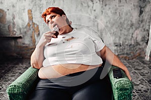 Overweight woman sits in chair and eats sweet cake