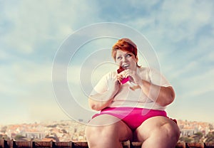 Overweight woman sits on roof and eats sweet cake