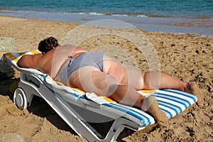 Overweight woman sunbathe on beach