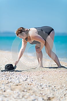 Overweight woman in swimsuit lifts off the ground hat