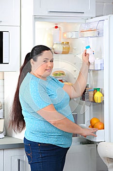 Overweight woman taking yogurt from refrigerator in kitchen