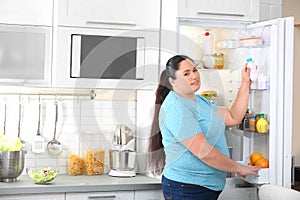 Overweight woman taking yogurt from refrigerator in kitchen, space for text.