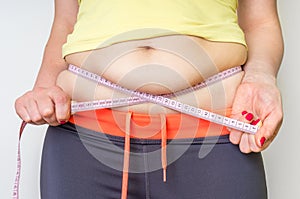 Overweight woman with tape is measuring fat on belly