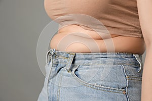 Overweight woman in tight jeans on grey background, closeup. Space for text