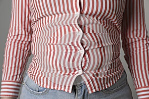 Overweight woman in tight shirt and jeans on grey background, closeup