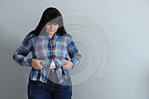 Overweight woman in tight shirt on light grey background. Space for text