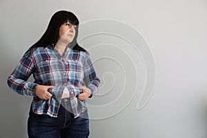 Overweight woman in tight shirt on light grey background. Space for text