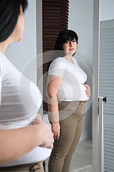 Overweight woman in tight t-shirt and trousers near mirror