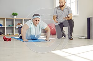 Overweight woman trying to do push ups during a fitness workout with a gym instructor
