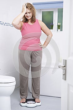Overweight Woman Weighing Herself On Scales In Bathroom photo