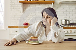 Overweight young woman hesitating to eat huge burger