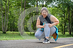 Overweight young woman with knee pain grabs her knee with both hands while sitting down at a running track of a local park