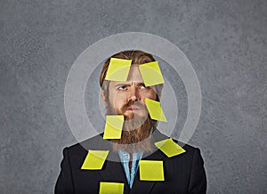 Overwhelmed bearded business man full of stickers looking up trying to remember his plans